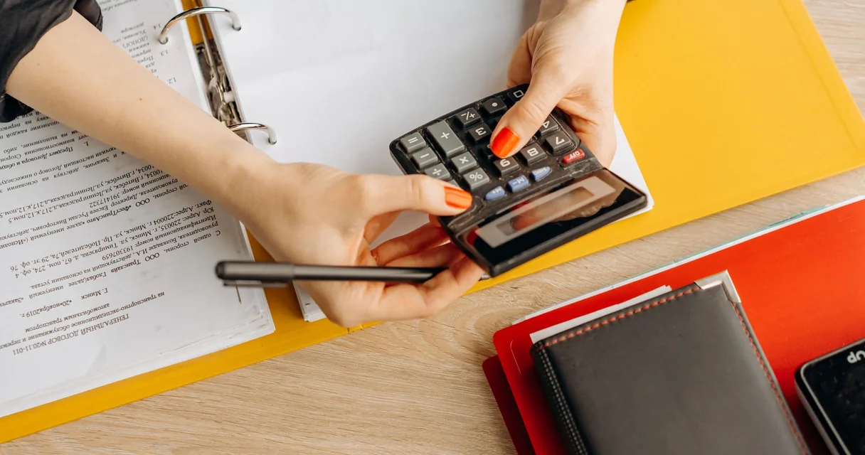 Mãos usando calculadora sobre pastas e documentos em uma mesa de escritório contábil