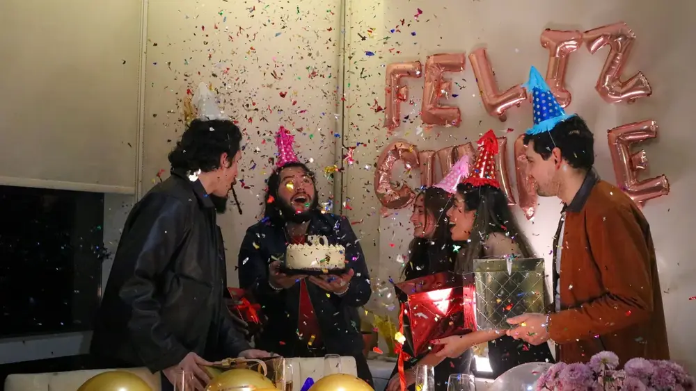 Amigos comemorando aniversário com bolo, chapéus de festa e confete