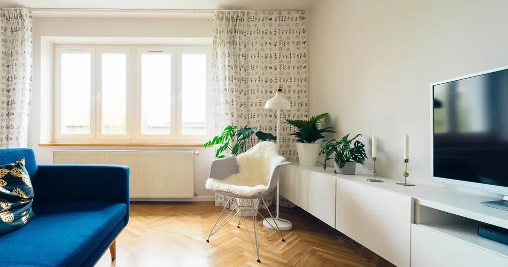 Sala de estar clara com sofá azul e televisão de tela plana